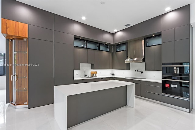 kitchen with wall chimney exhaust hood, sink, a center island, light tile patterned floors, and black electric stovetop