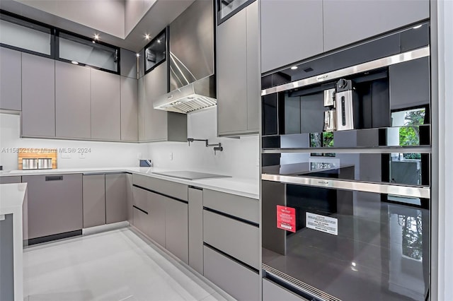 kitchen with gray cabinets, double wall oven, black electric cooktop, and wall chimney exhaust hood