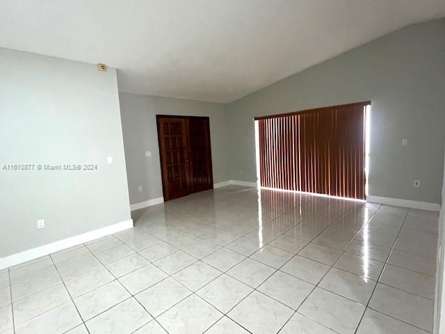 tiled spare room featuring vaulted ceiling