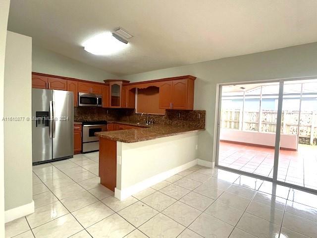 kitchen with dark stone counters, vaulted ceiling, light tile flooring, backsplash, and appliances with stainless steel finishes