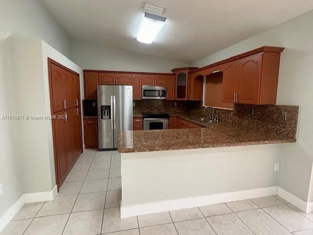 kitchen with lofted ceiling, stainless steel appliances, a peninsula, a sink, and backsplash