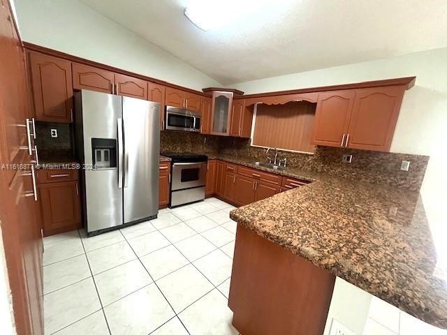 kitchen with backsplash, appliances with stainless steel finishes, light tile floors, and lofted ceiling