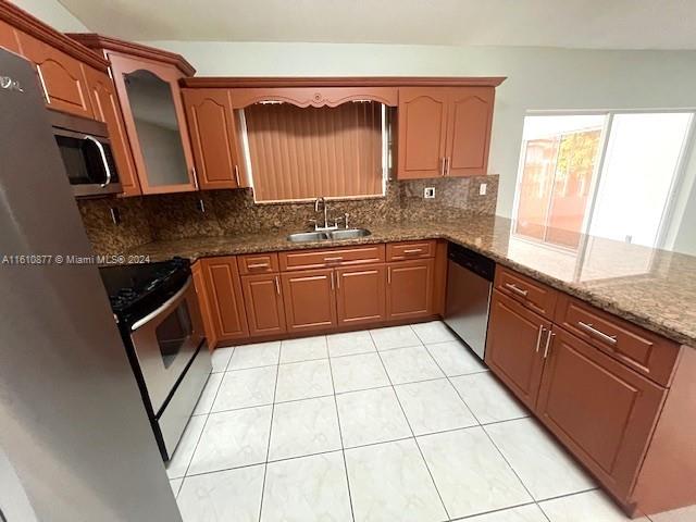 kitchen featuring appliances with stainless steel finishes, backsplash, stone counters, sink, and light tile floors