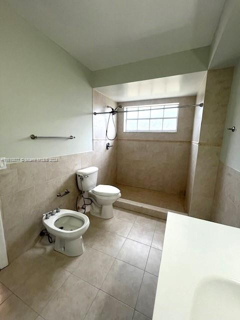 bathroom with tile walls, toilet, a bidet, tile patterned flooring, and tiled shower