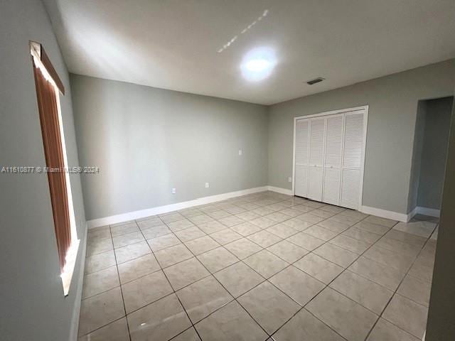 unfurnished bedroom with light tile patterned floors, a closet, visible vents, and baseboards