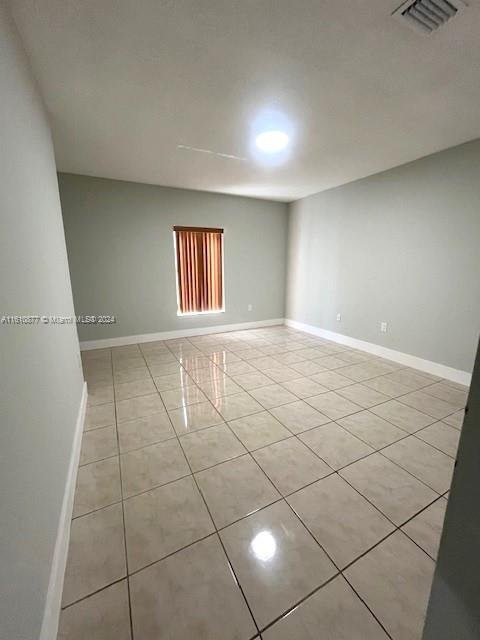 empty room with light tile patterned floors, visible vents, and baseboards