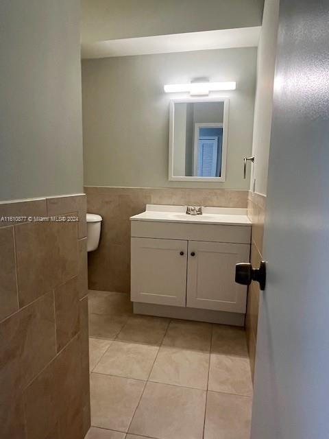 bathroom with tile floors, tile walls, toilet, and vanity