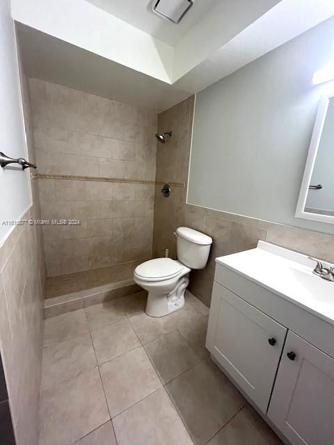 bathroom featuring tiled shower, tile floors, tile walls, vanity, and toilet