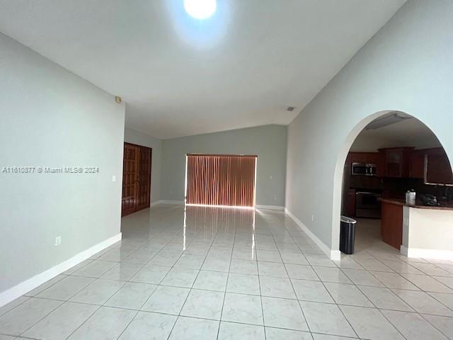 tiled empty room featuring lofted ceiling