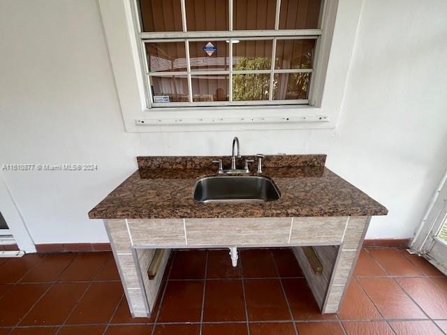 kitchen featuring dark stone counters, dark tile patterned flooring, a sink, and baseboards