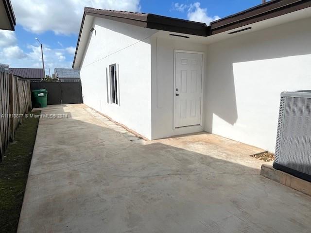 view of exterior entry with a patio, fence, cooling unit, and stucco siding