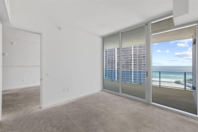 carpeted spare room featuring a view of the beach, expansive windows, and a water view