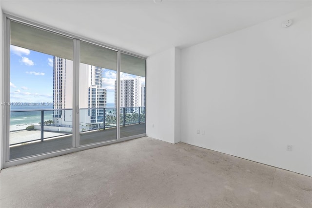 carpeted empty room with a view of the beach, a healthy amount of sunlight, expansive windows, and a water view