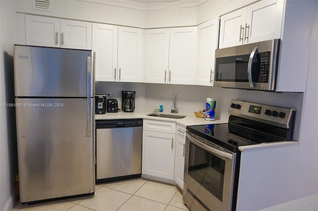 kitchen with appliances with stainless steel finishes, sink, light tile patterned floors, and white cabinets