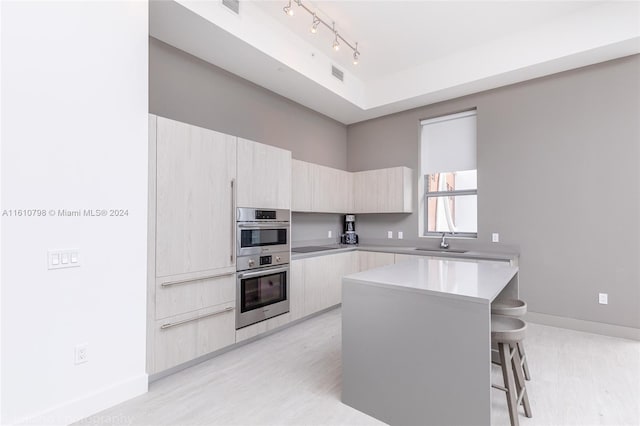 kitchen with light wood-type flooring, track lighting, sink, stainless steel double oven, and a breakfast bar area