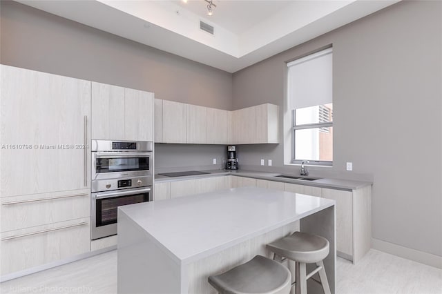 kitchen featuring black electric stovetop, a kitchen island, stainless steel double oven, sink, and a kitchen bar