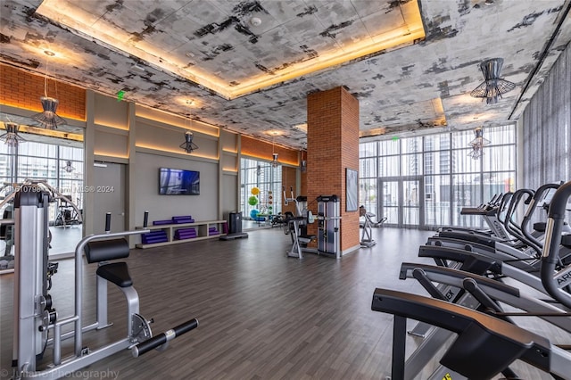 exercise room featuring dark hardwood / wood-style floors, ceiling fan, expansive windows, a raised ceiling, and brick wall