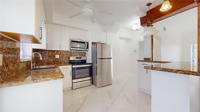 kitchen with appliances with stainless steel finishes, tasteful backsplash, white cabinetry, sink, and decorative light fixtures