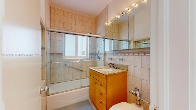 full bathroom featuring combined bath / shower with glass door, toilet, vanity, and tile walls