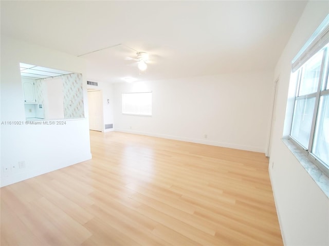 empty room with visible vents, light wood-style flooring, a ceiling fan, and baseboards