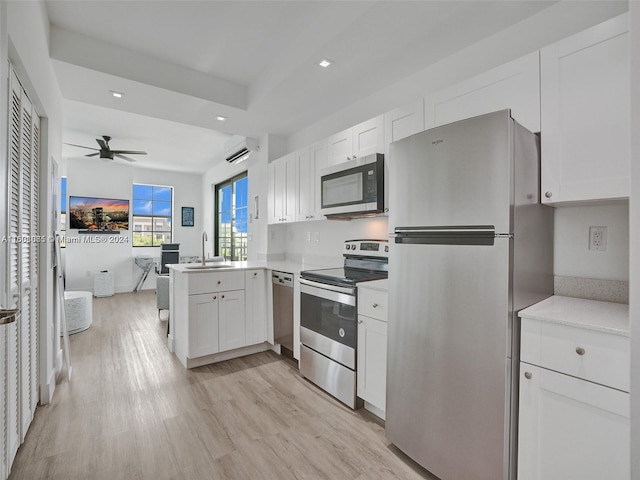 kitchen with appliances with stainless steel finishes, open floor plan, white cabinets, a sink, and a peninsula