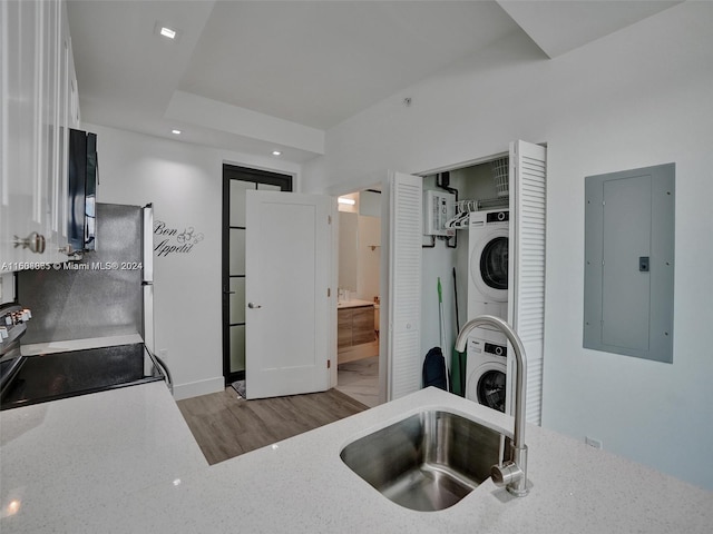 kitchen featuring stacked washer and dryer, electric panel, white cabinets, light wood-style flooring, and stainless steel range with electric stovetop