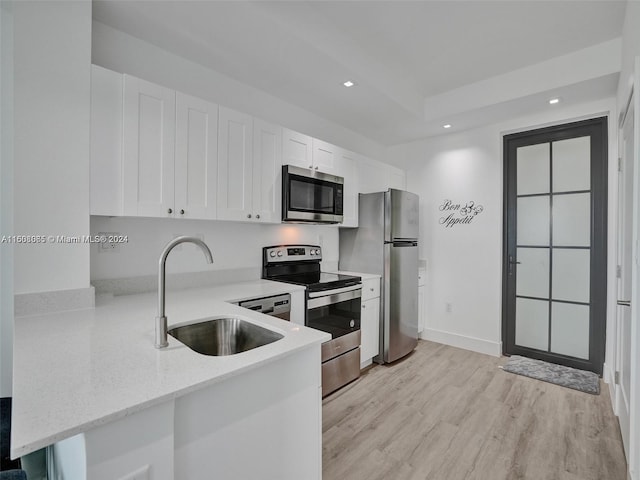 kitchen featuring stainless steel appliances, light wood-style flooring, white cabinets, a sink, and a peninsula