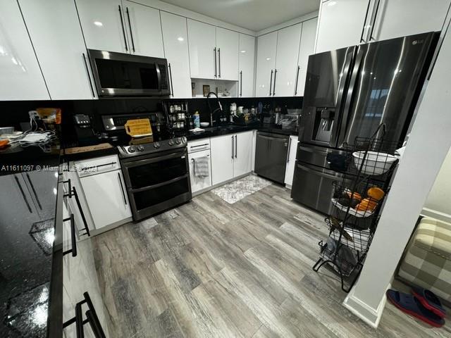 kitchen featuring electric stove, dishwashing machine, white cabinetry, and light hardwood / wood-style flooring