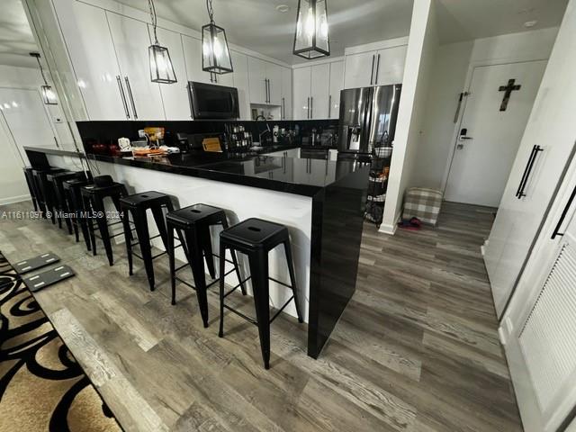 kitchen with kitchen peninsula, decorative light fixtures, dark hardwood / wood-style flooring, a breakfast bar area, and white cabinetry