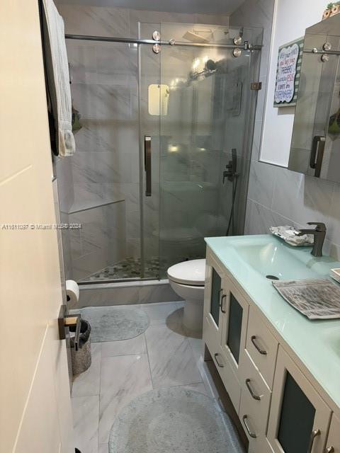 bathroom featuring tile walls, toilet, tile flooring, an enclosed shower, and vanity