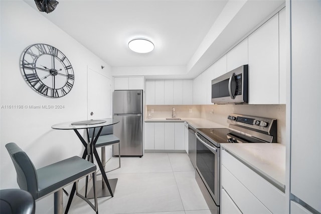 kitchen with white cabinets, sink, decorative backsplash, light tile patterned floors, and appliances with stainless steel finishes