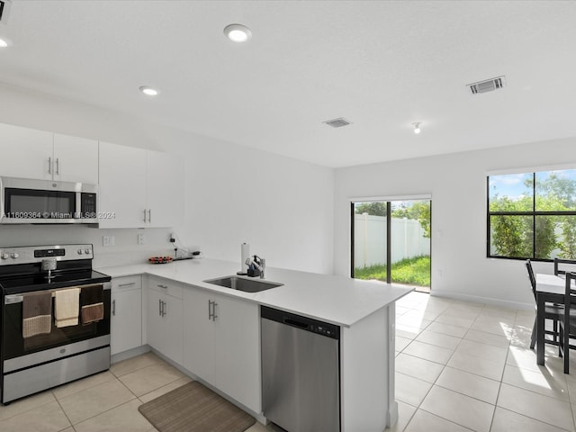 kitchen with kitchen peninsula, light tile floors, sink, white cabinetry, and appliances with stainless steel finishes