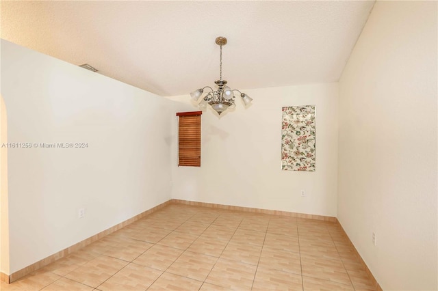 tiled spare room featuring a textured ceiling and a notable chandelier