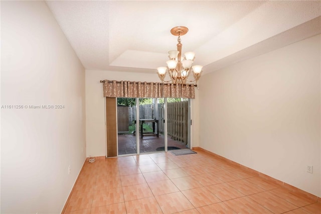 unfurnished room featuring a raised ceiling, tile patterned flooring, and a chandelier