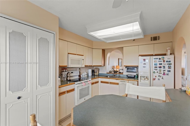 kitchen with sink, kitchen peninsula, cream cabinetry, and white appliances