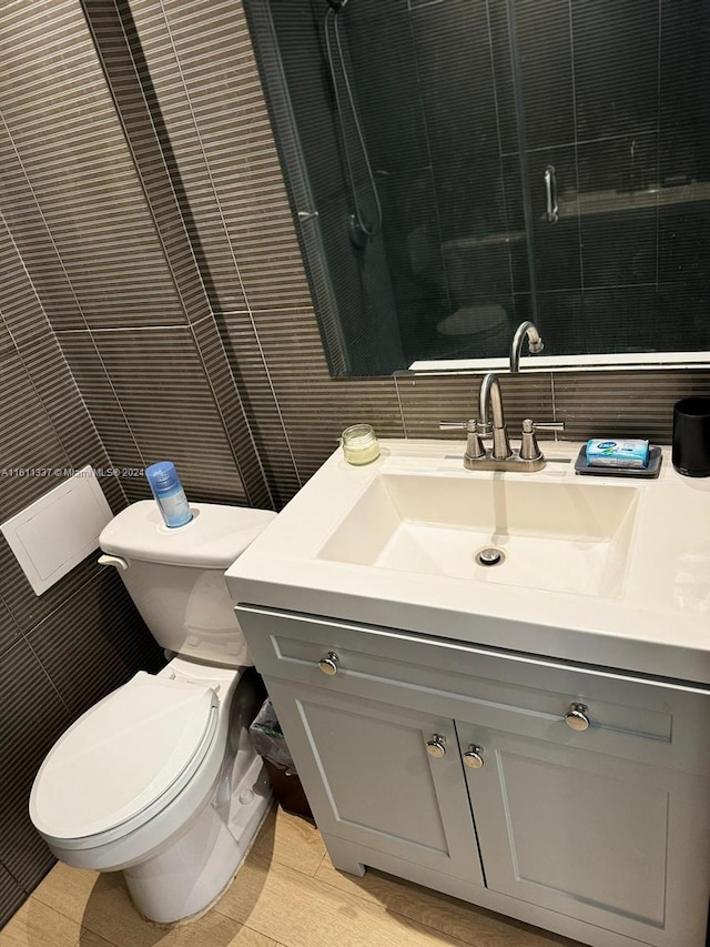 bathroom with vanity, a shower, tile walls, and toilet