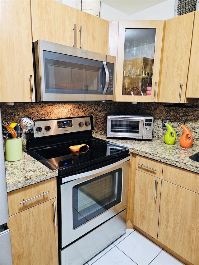 kitchen featuring light stone countertops, light brown cabinets, tasteful backsplash, light tile patterned floors, and appliances with stainless steel finishes