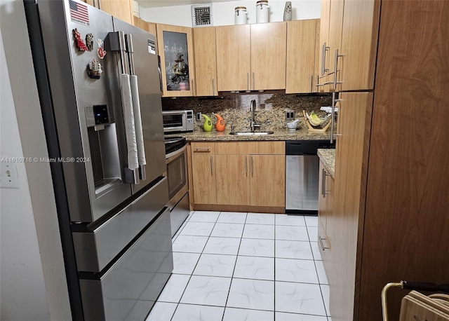 kitchen featuring light stone countertops, decorative backsplash, stainless steel appliances, and sink