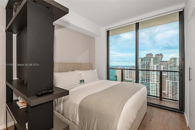 bedroom with a wall of windows, access to exterior, a water view, and light wood-type flooring