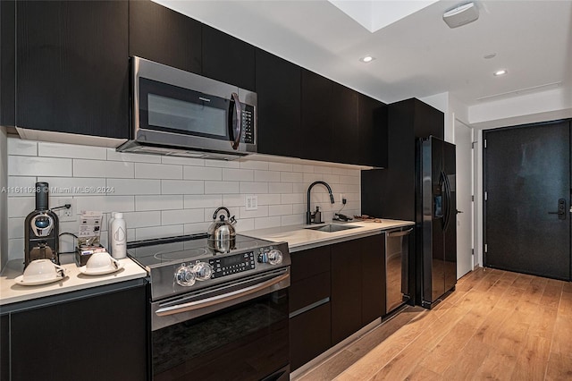 kitchen featuring a skylight, sink, tasteful backsplash, light hardwood / wood-style flooring, and appliances with stainless steel finishes