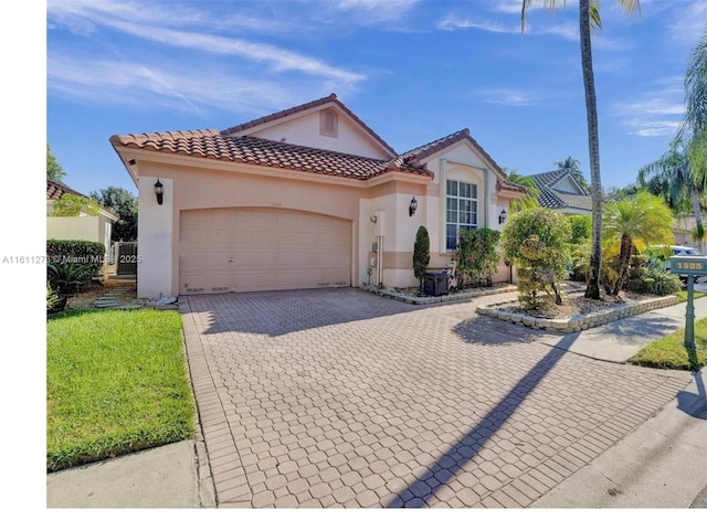 mediterranean / spanish-style house with decorative driveway, a tile roof, an attached garage, and stucco siding