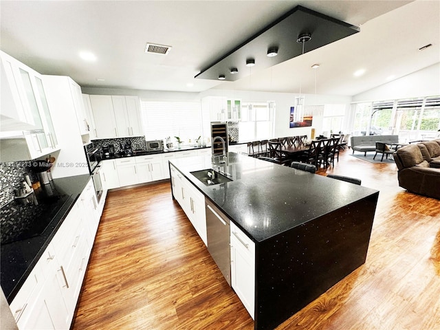 kitchen with black electric stovetop, light wood-style floors, tasteful backsplash, and visible vents