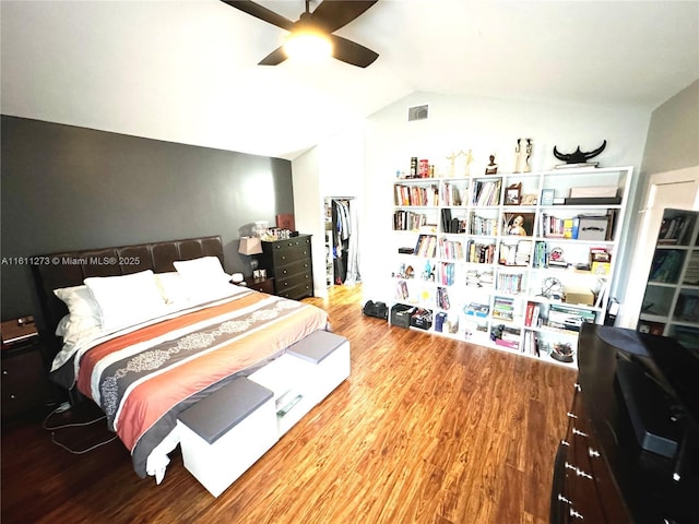 bedroom featuring a walk in closet, visible vents, ceiling fan, vaulted ceiling, and wood finished floors