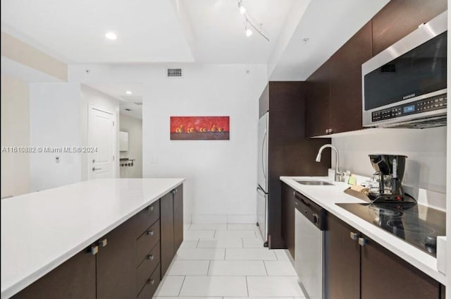 kitchen with stainless steel appliances, dark brown cabinetry, sink, track lighting, and light tile flooring