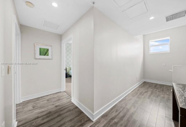 hall with baseboards, attic access, visible vents, and wood finished floors