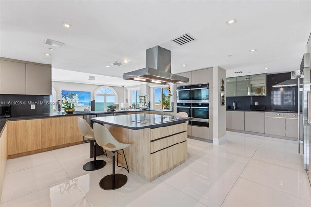 kitchen featuring a breakfast bar area, black appliances, island exhaust hood, light tile patterned flooring, and a spacious island