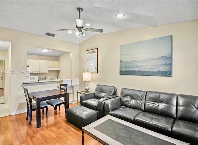 living room with lofted ceiling, light hardwood / wood-style flooring, ceiling fan, and a textured ceiling