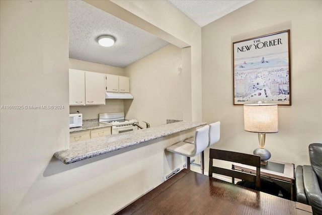 kitchen featuring white cabinetry, light stone countertops, white appliances, and a textured ceiling