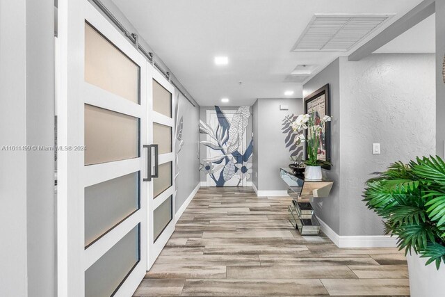 corridor with a barn door and light hardwood / wood-style floors