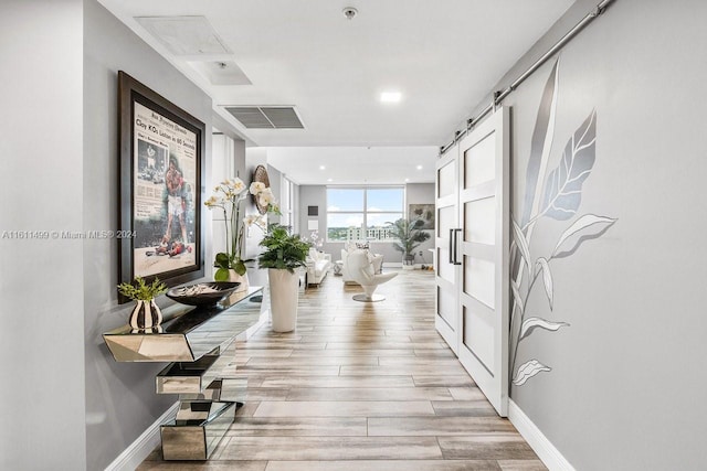 corridor featuring a barn door, recessed lighting, visible vents, baseboards, and light wood-type flooring